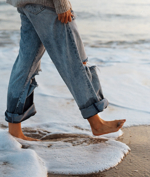 Woman walking barefoot through ocean wave foam on the beach
